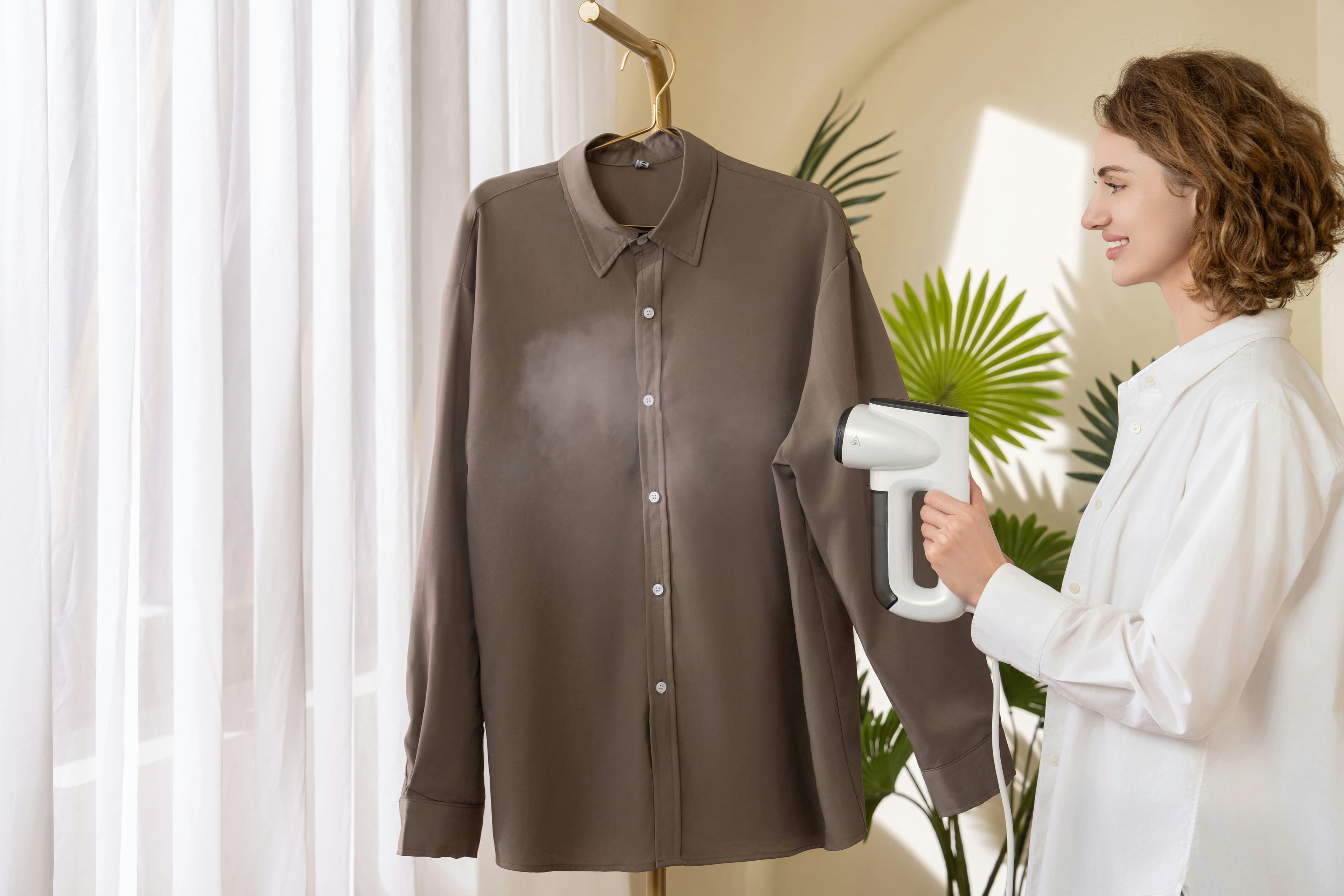 A shirt on a hanger being smoothed with a handheld garment steamer